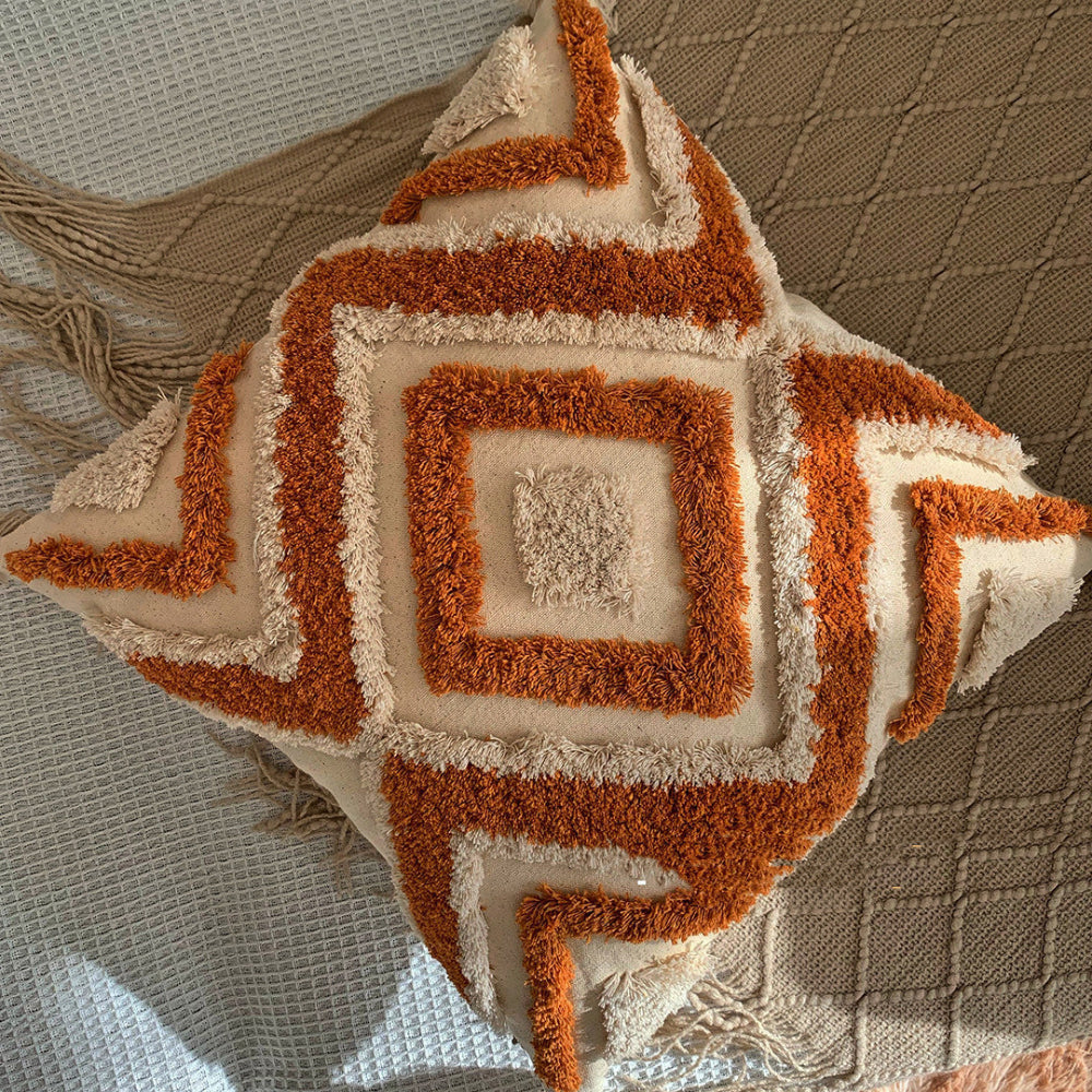 Beige and orange textured pillow on a blanket with tassels and on a white fabric textured surface. Scandinavian interior with warm light. 