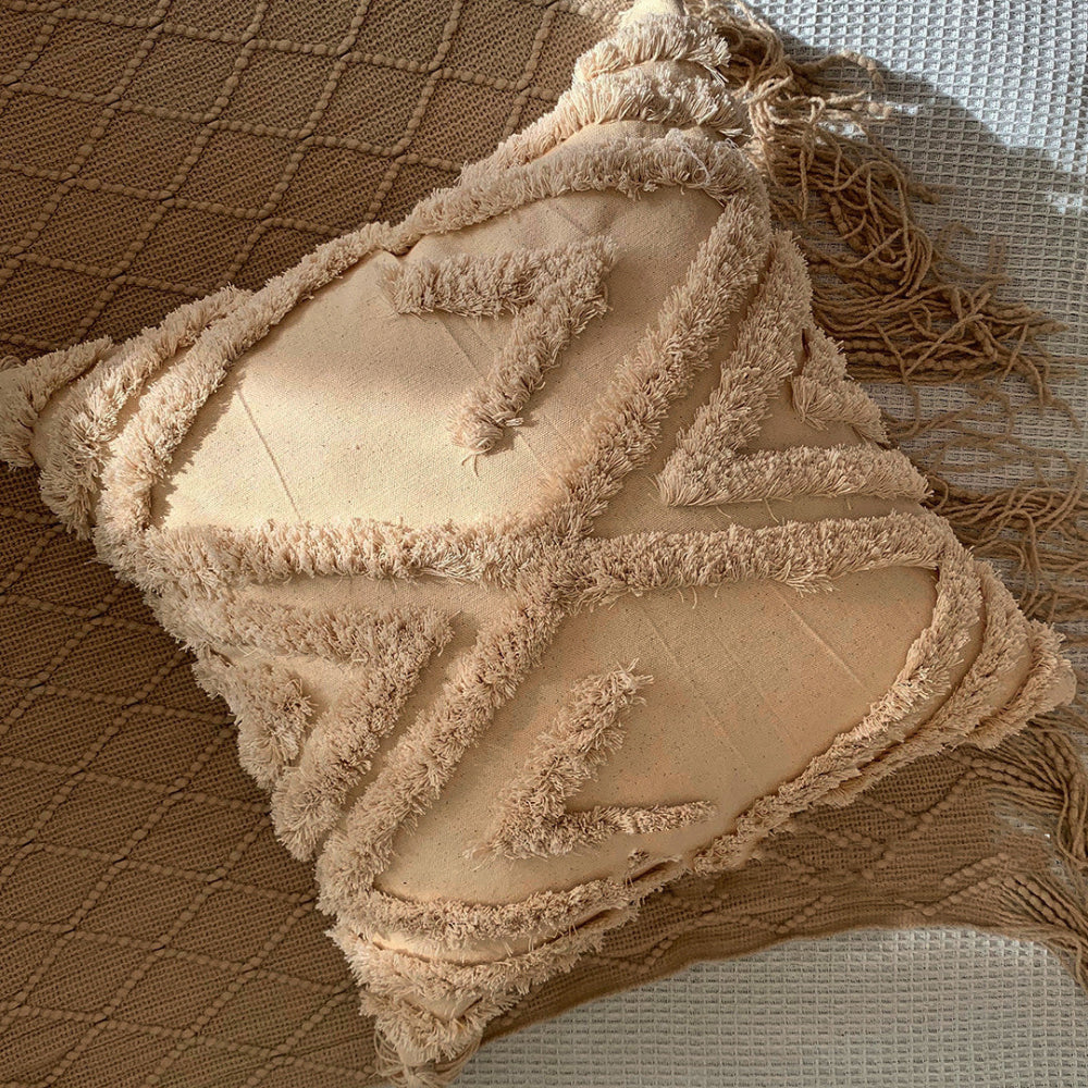 Beige textured pillow on a blanket with tassels and on a white fabric textured surface. Scandinavian interior with beige and warm light. 