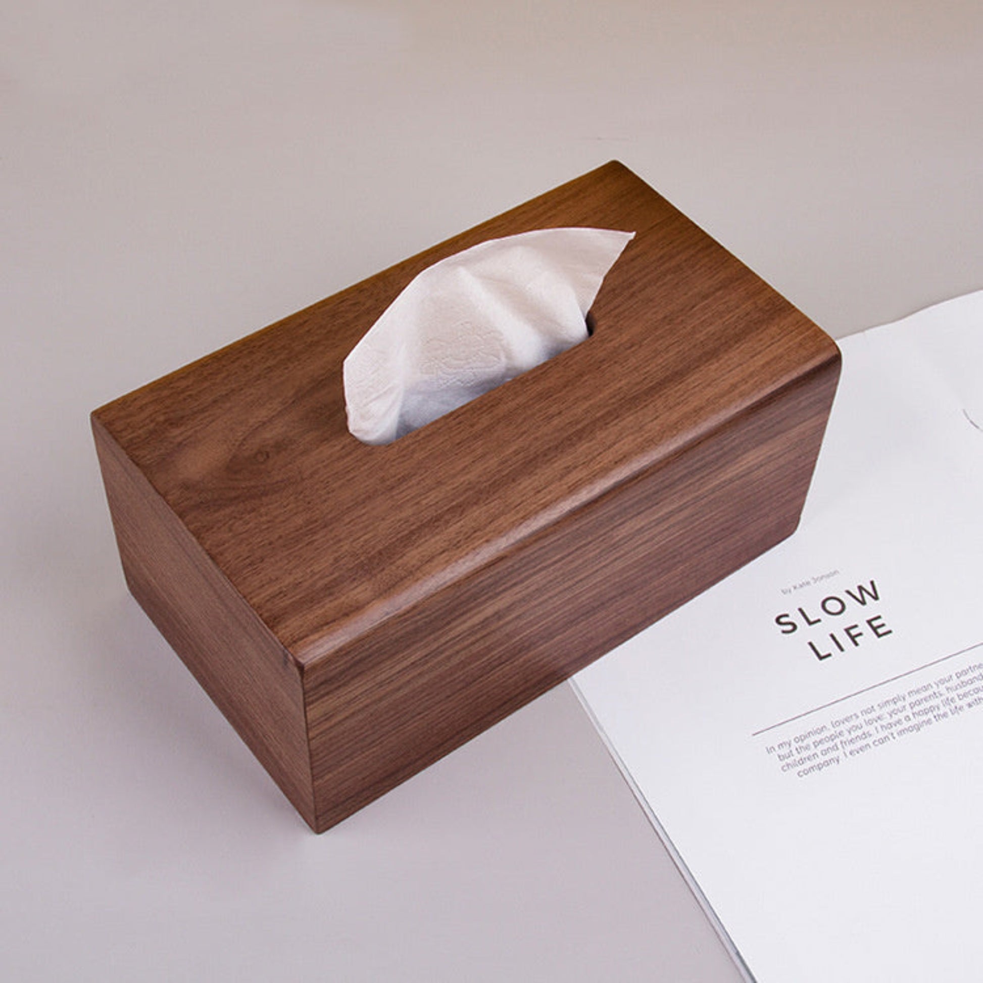 Natural walnut tissue box with warm earthy tones and organic materials on a white surface and on a book. Perfect for a minimalist interior atmosphere. Walnut Tissue Box. 