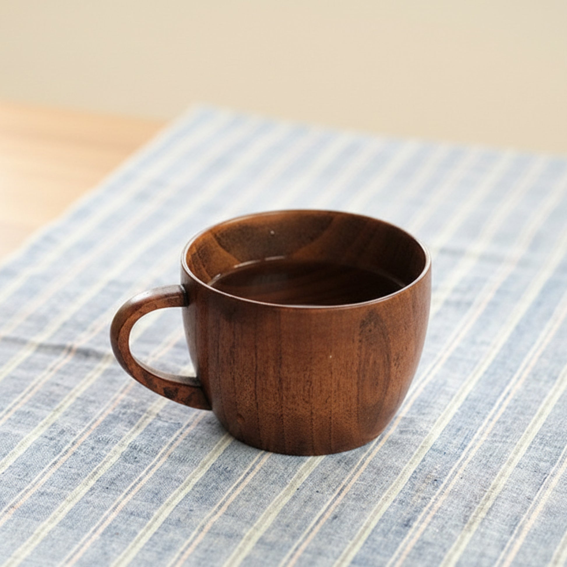 Whole wood mug on a beige surface on a striped fabric background. Nature inspired and warm natural decor styling. 