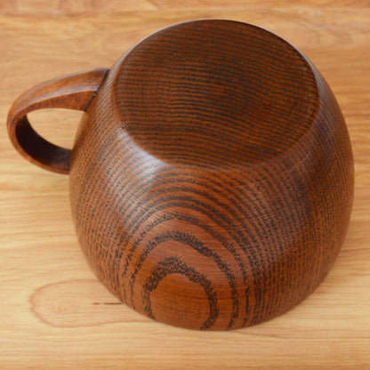 Whole wood mug on a wooden surface. Bottom pictured. Nature inspired and warm natural decor styling. 