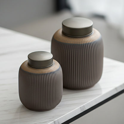 Two ribbed ceramic jars with metallic lids on a light gray marble surface. Grey-brown earthy and warm kitchen item. Minimalist home decor and tea storage. 