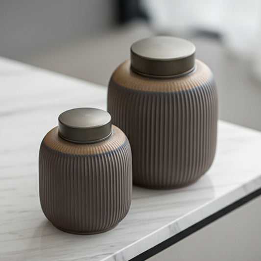 Two ribbed ceramic jars with metallic lids on a light gray marble surface. Grey-brown earthy and warm kitchen item. Minimalist home decor and tea storage. 