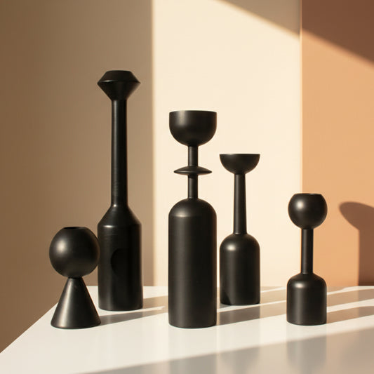 Set of five black wooden candle holders on a white surface and earthy, warm background. Natural light shines on the five black candle holders. 