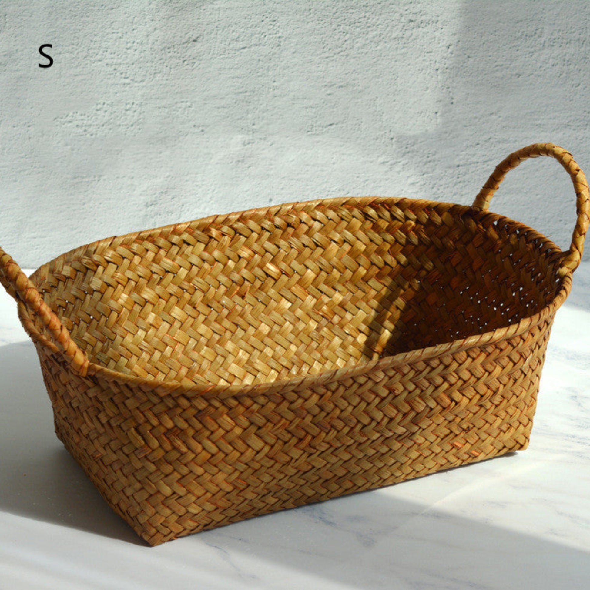 Woven basket with handles on a light background and on a light grey marble surface. Size S. 
Scandinavian decor inspired by simplicity and warm tones. Perfect for creating calm, minimalist interiors. Earthy tones for storage. 
