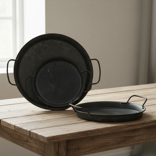Three wrought iron trays with handles on a wooden table and a blurred white-beige background. Minimalist black decor centerpiece. 