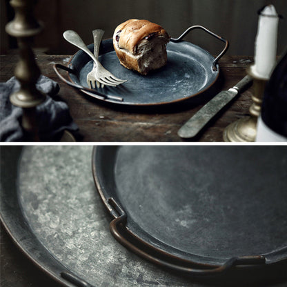Wrought iron trays with handles on a wooden surface. On one tray is a chocolate bread with two forks. Minimalist black decor centerpiece. 